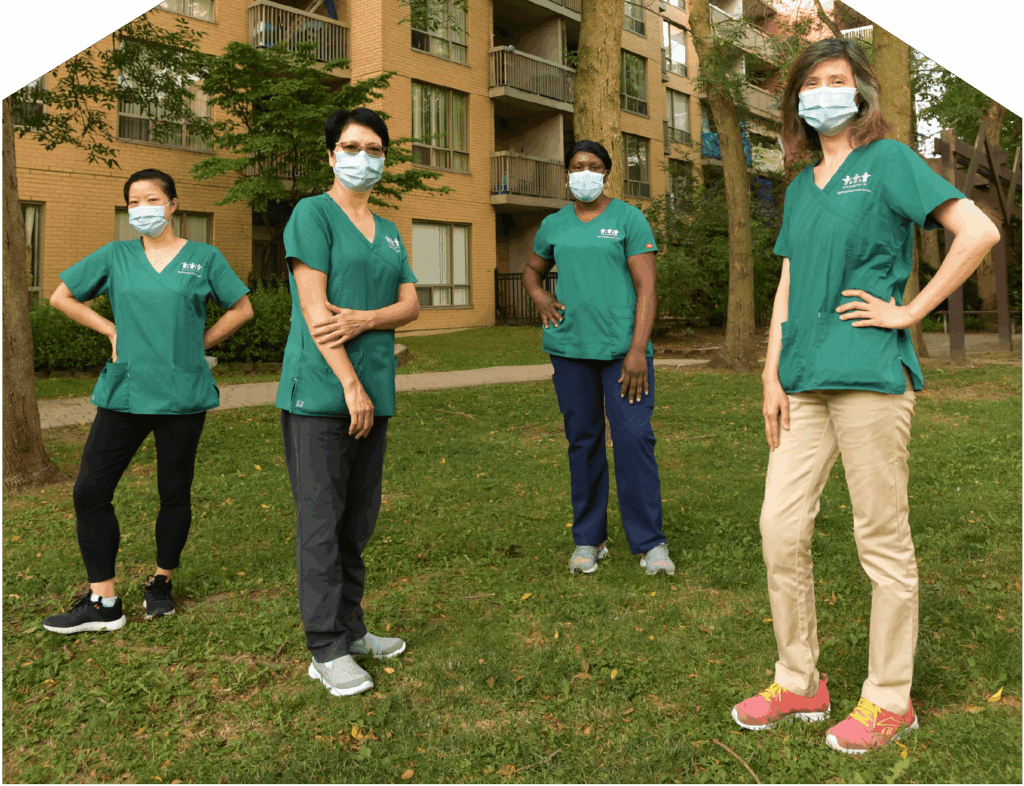 our WoodGreen Personal Support Workers wearing masks and physically distanced from each other, standing outside a building surrounded by trees.