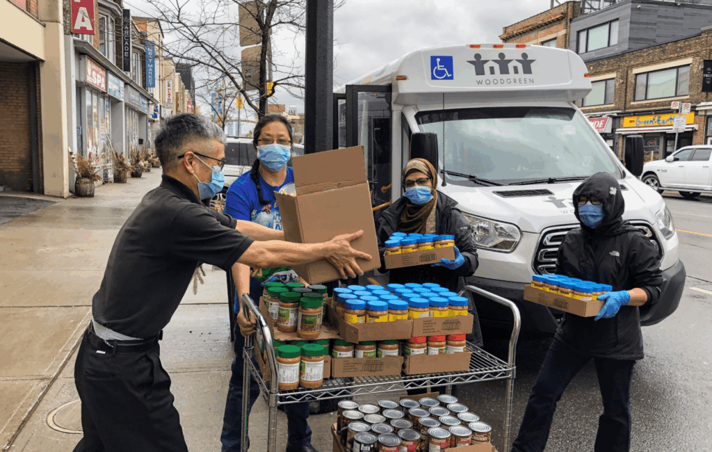 Four people wearing masks on the street loading non-perishable food items into a WoodGreen vehicle