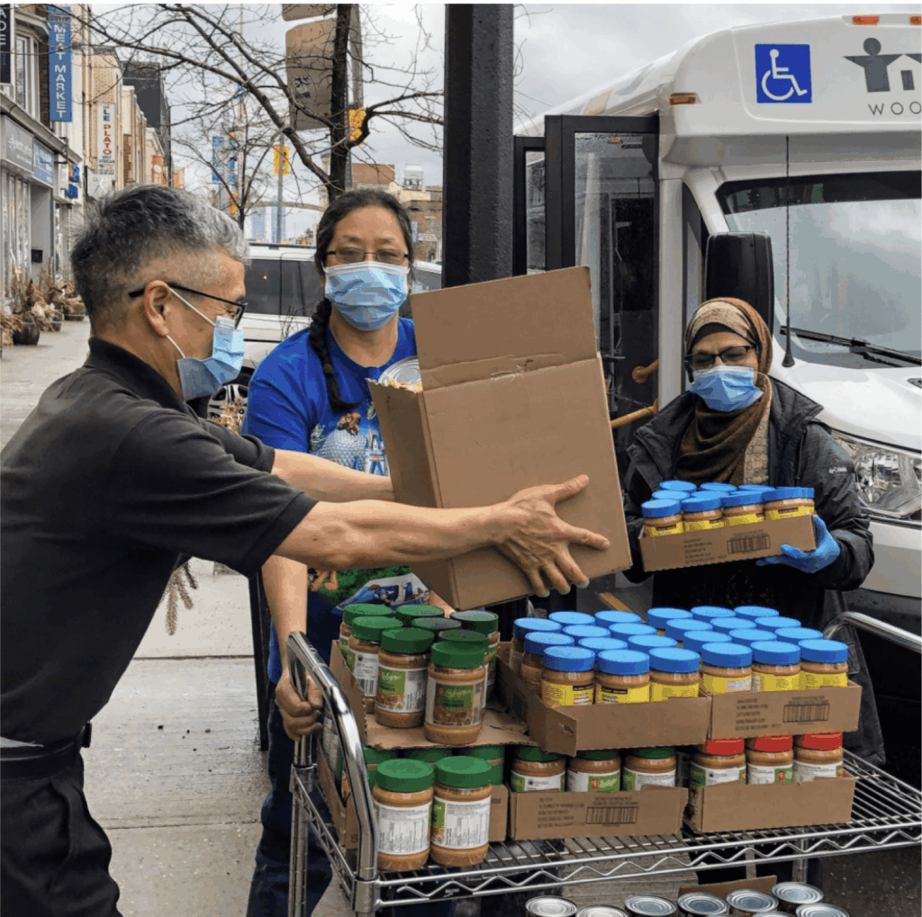 Four people wearing masks on the street loading non-perishable food items into a WoodGreen vehicle