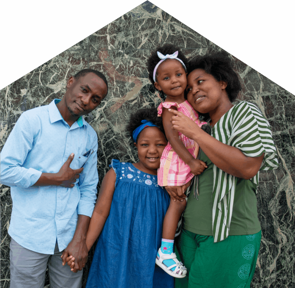 A family, mother, father and two daughters, standing close to each other in front of a WoodGreen building.