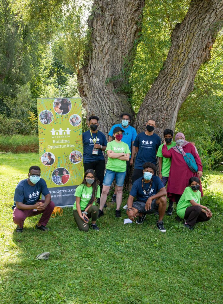 A group of 10 people standing outside in front of a tree, all wearing masks and in different poses.