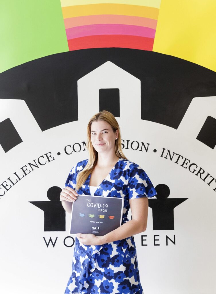 WoodGreen staff standing in front of a bright rainbow mural, holding a printed report in her hands.