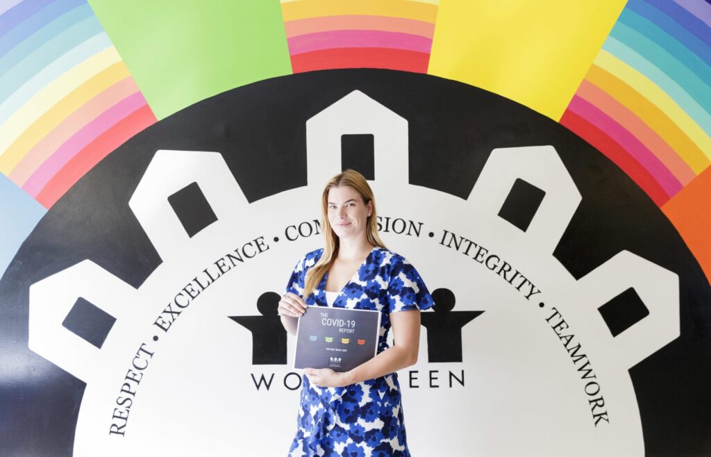 WoodGreen staff standing in front of a bright rainbow mural, holding a printed report in her hands.