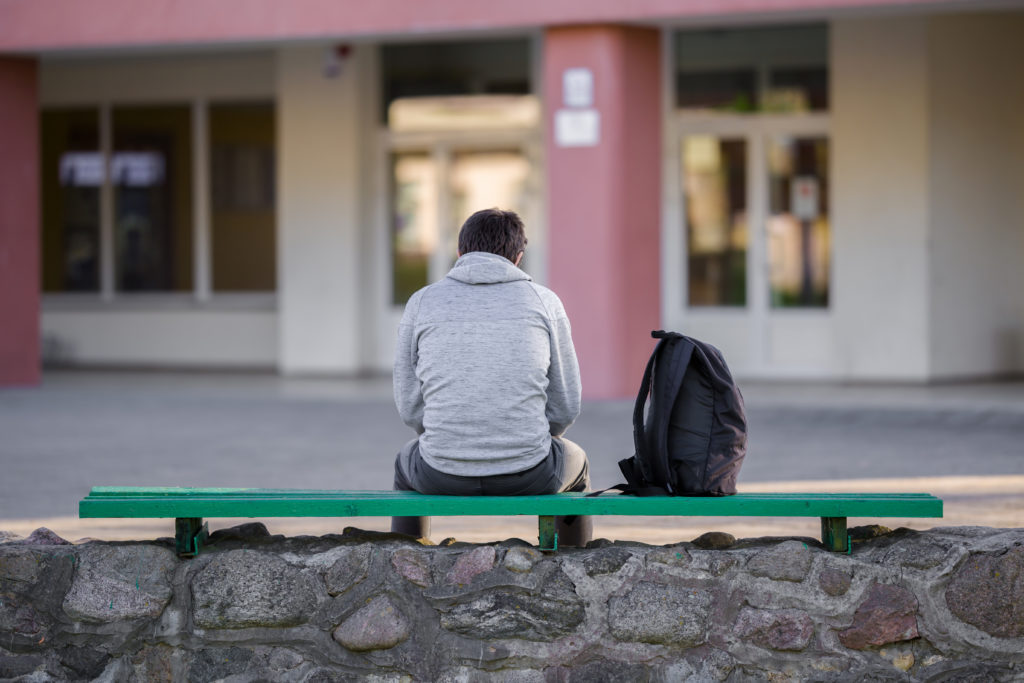 One young man sitting on bench at school yard. Break time. Back view.