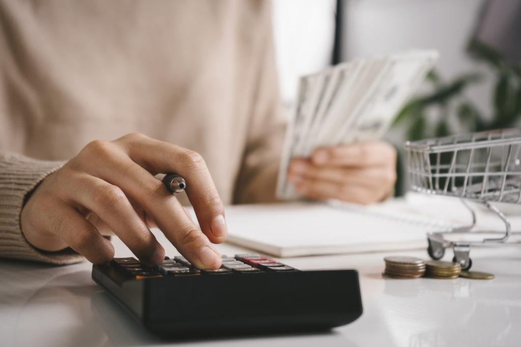 Woman counting and calculate cost money with calculator at home. Budget of disadvantaged and low income family for rising food and grocery store prices and expensive daily consumer goods concept.