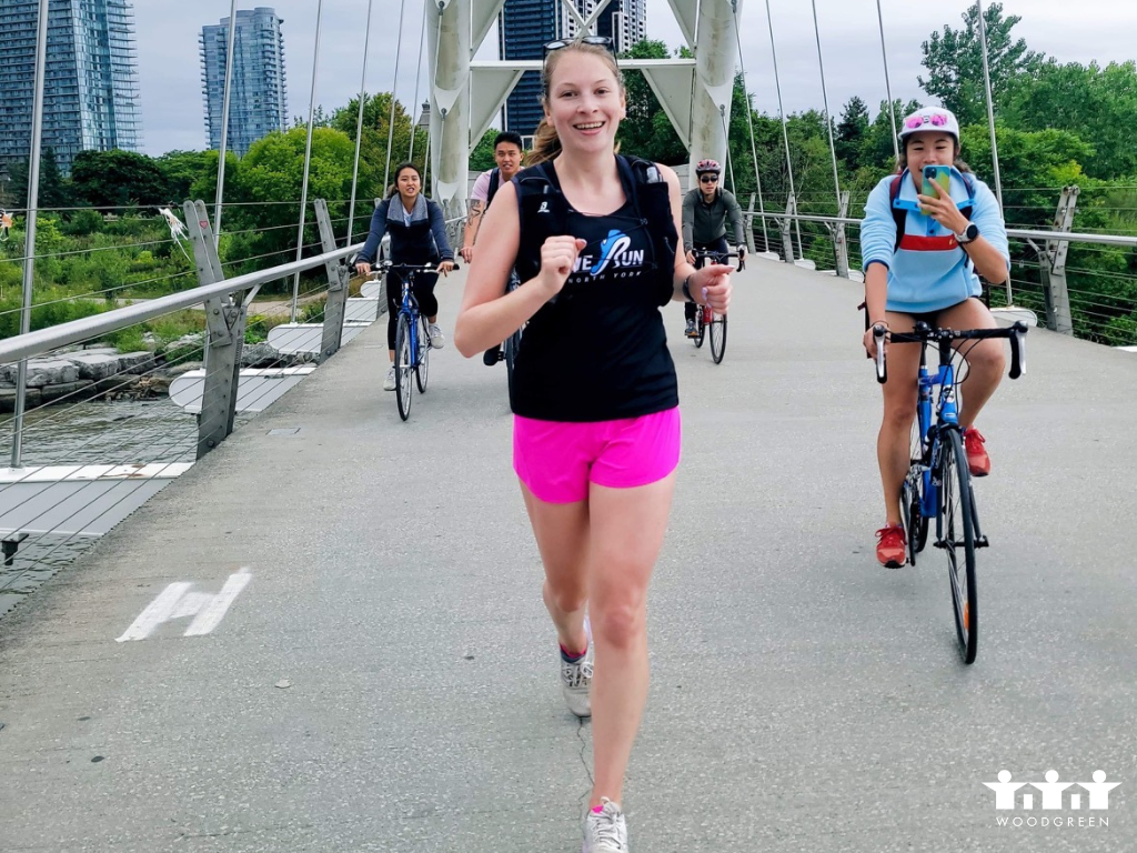 A woman in pink shorts and a black tshirt is running across a bridge.