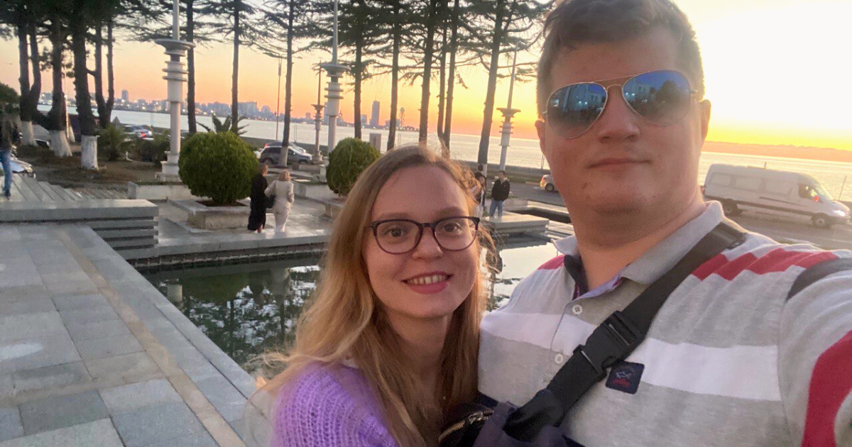 a man wearing sunglasses and a woman stand in front of trees and water in Ukraine