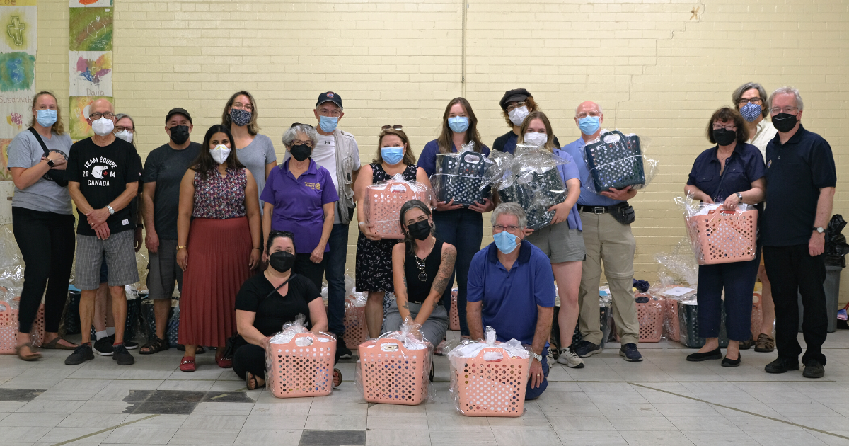 a group of about 20 people stands with welcome baskets in a church basement