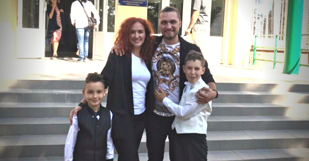 a man, woman and two young boys stand in front of stairs outdoors in Ukraine