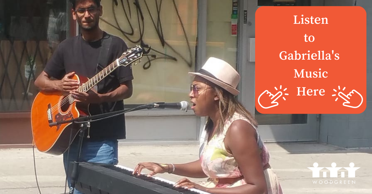 A woman sits at a keyboard and plays music outside in the street while a man in a black shirt stands and plays guitar. 