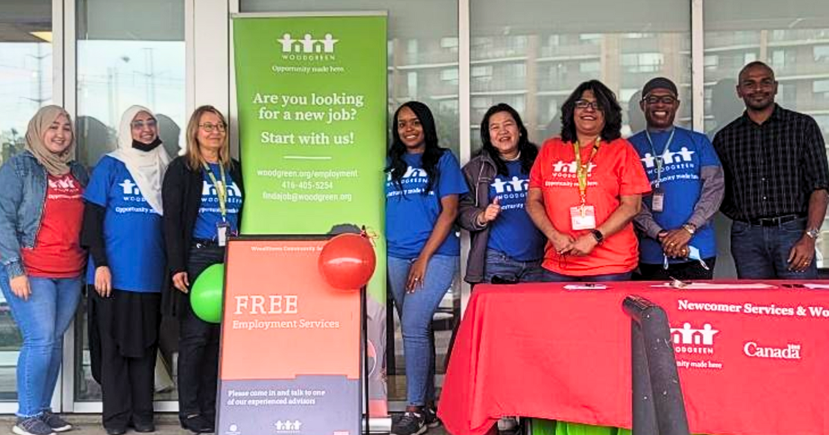 a group of workers at Employee Services WoodGreen wear bright blue and red shirts while standing in front of a building