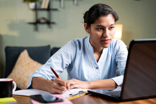 Female writing notes and using laptop and staring at computer screen.